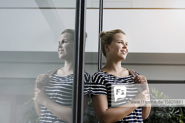 Porträt einer lächelnden jungen Frau im Büro  die sich in einer Glasscheibe spiegelt