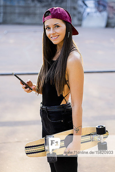 Junge Frau mit Smartphone und Skateboard im Skatepark