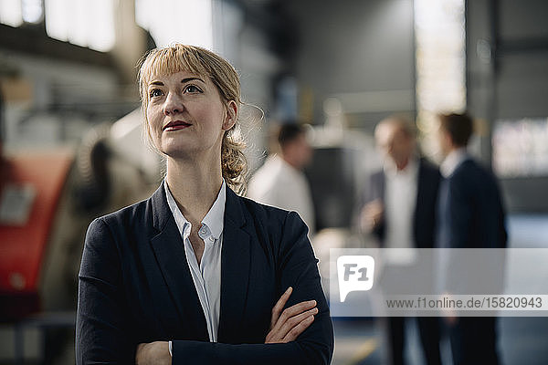 Porträt einer selbstbewussten Geschäftsfrau in einer Fabrik mit Kollegen im Hintergrund