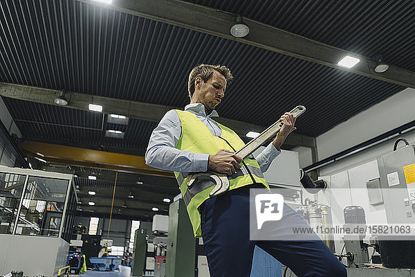 Man wearing reflective vest in a factory playing air guitar on large wrench