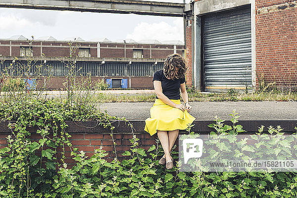 Frau sitzt auf einer mit Pflanzen bewachsenen Wand in einem alten Industriegebiet
