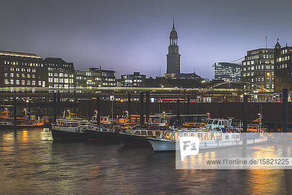 Germany  Hamburg  Boats moored in city harbor at dusk with light trail and tower of Saint Michaels Church in background