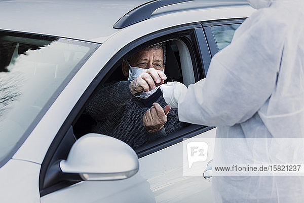 Mann in Schutzkleidung kontrolliert älteren Mann im Auto