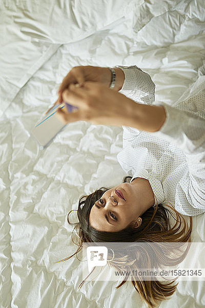 Geschäftsfrau liegt im Bett und benutzt Mobiltelefon