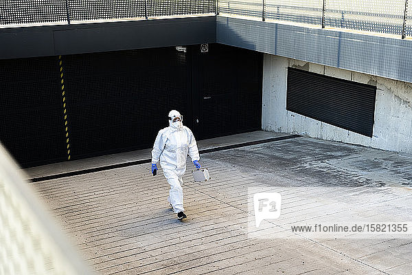 Wissenschaftlerin  die Schutzanzug und Maske trägt und in eine Garage geht
