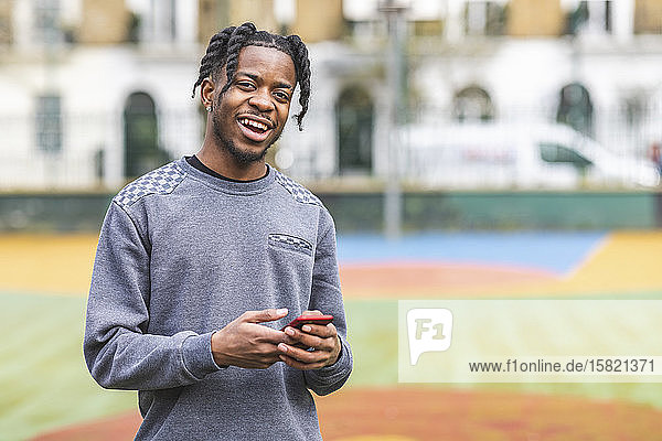 Laughing young man holding smartphone  looking at camera