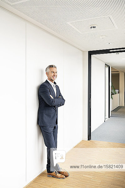 Businessman corridor of office building  leaning on wall  with arms crossed
