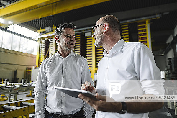 Zwei Geschäftsleute mit Tablette im Gespräch in einer Fabrik