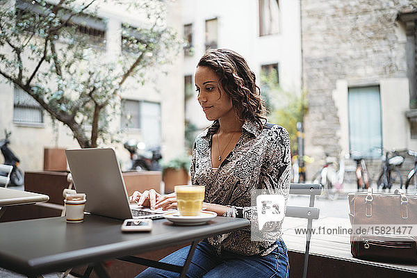 Junge Frau mit Laptop in einem Straßencafé