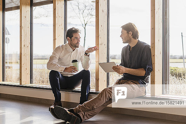 Zwei Geschäftsleute mit Tablett am Fenster im Großraumbüro im Gespräch