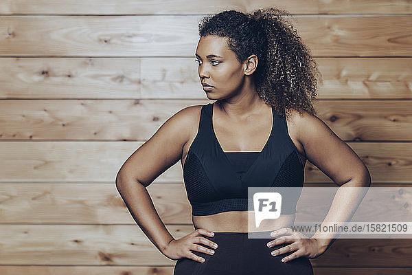 Porträt einer selbstbewussten  sportlichen jungen Frau an einer Holzwand stehend