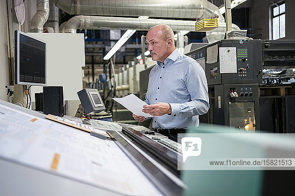Businessman holding paper at a machine in a factory