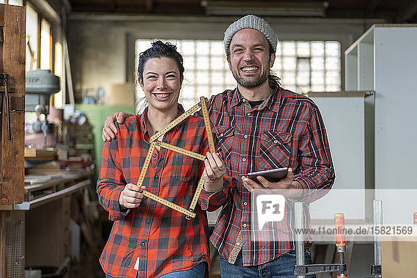 Porträt einer glücklichen Handwerkerin und eines Handwerkers  die in ihrer Werkstatt Tafel und Messlatte halten