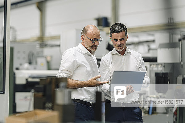 Two businessmen using laptop in a factory