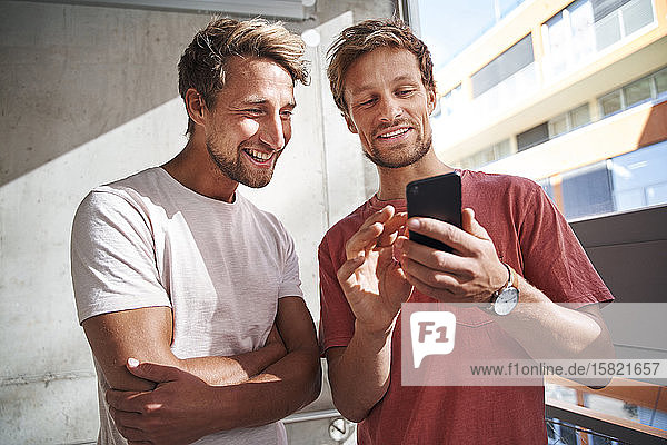 Two happy young men sharing smartphone