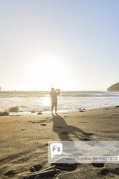 Man standing on the beach at sunset taking pictures  Sao Miguel Island  Azores  Portugal