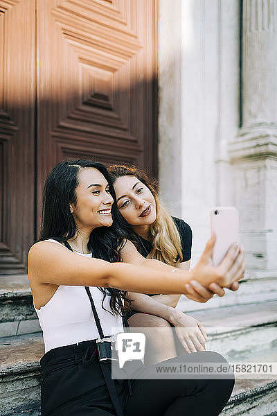 Porträt von zwei Freunden  die auf einer Treppe sitzen und sich mit einem Smartphone selbstständig machen  Lissabon  Portugal