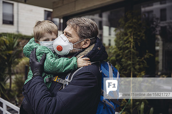 Father carrying son both wearing protective maska outdoors