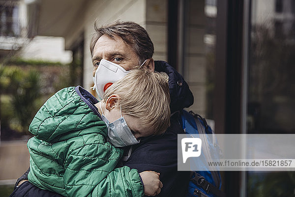 Father carrying son both wearing protective maska outdoors