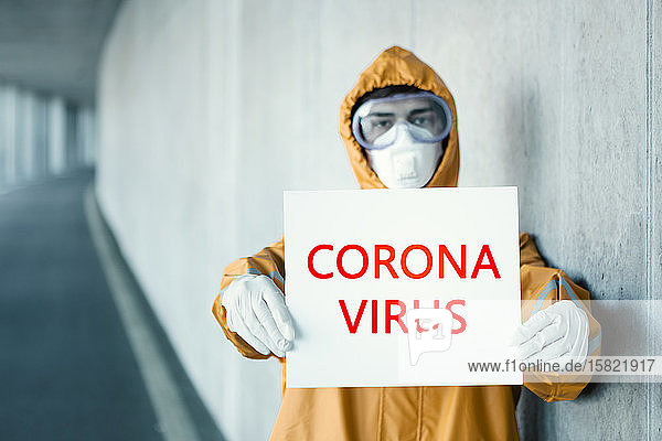 Porträt eines Mannes in Schutzkleidung mit Corona-Virus -Schild