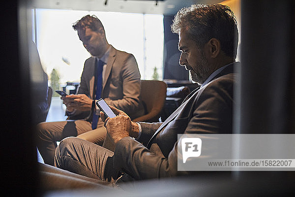 Zwei Geschäftsleute benutzen Smartphones in der Hotellobby