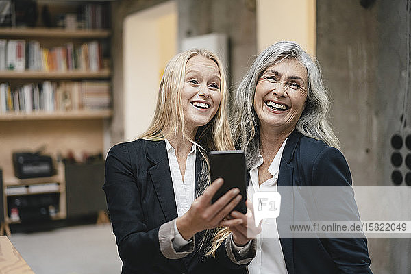 Glückliche reife und junge Geschäftsfrau nutzt Smartphone im Loft-Büro