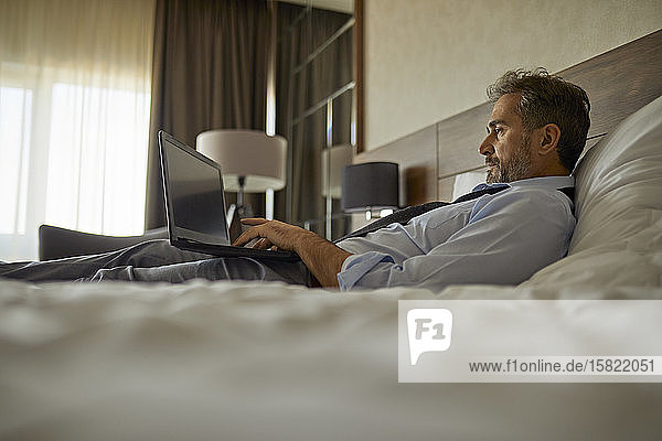 Geschäftsmann im Hotelzimmer auf dem Bett liegend mit Laptop