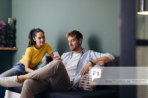 Young couple sitting on the couch at home looking at smartphone