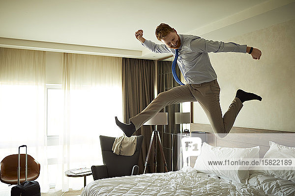 Aufgeregter Geschäftsmann springt im Hotelzimmer aufs Bett