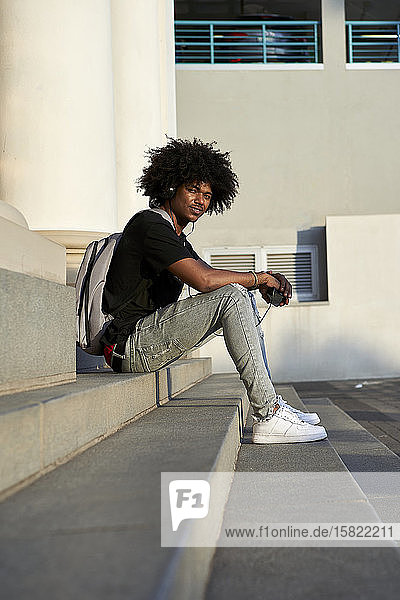Junger Mann hört Musik  hält sein Smartphone in der Hand  sitzt auf der Treppe