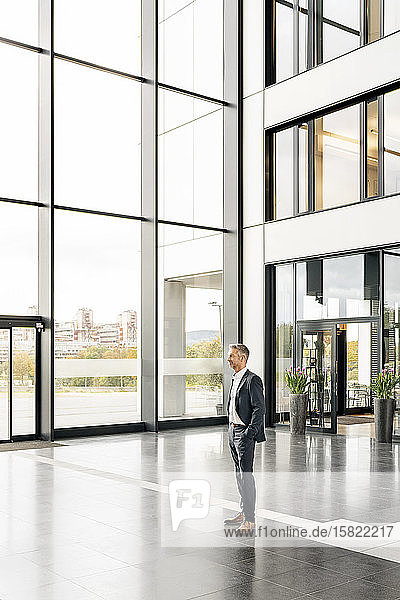 Successful businessman standing in entrance hall of office building  with hands in pockets