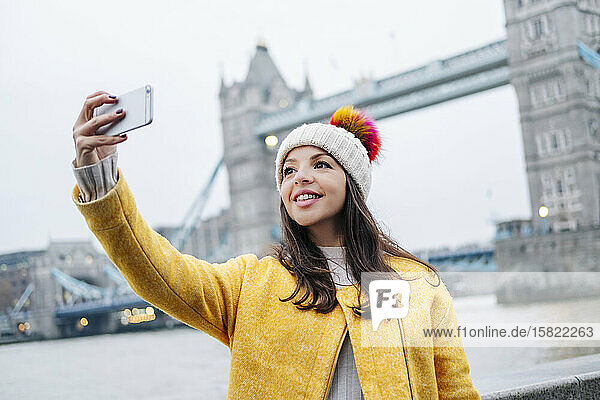 Zwei junge Touristen sitzen mit einem Smartphone an der Wand mit der London Bridge im Hintergrund