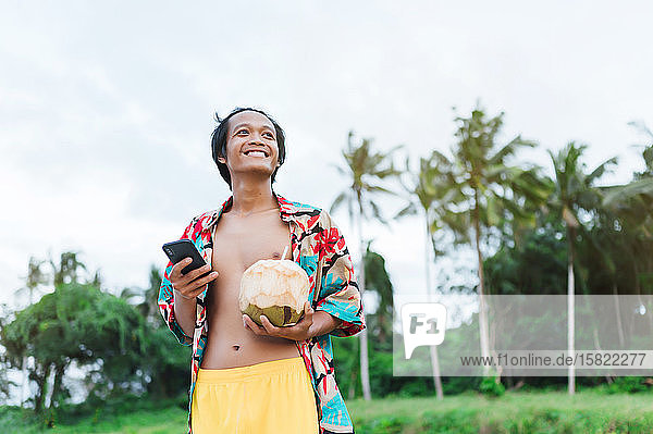 Porträt eines glücklichen Mannes mit Smartphone und frischer Kokosnuss  Insel Borneo  Malaysia