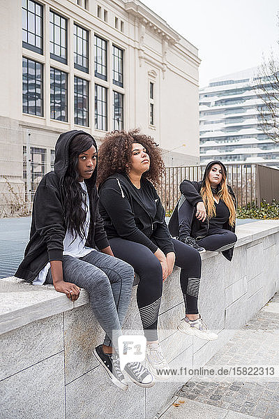 Drei sportliche junge Frauen sitzen auf einer Mauer in der Stadt