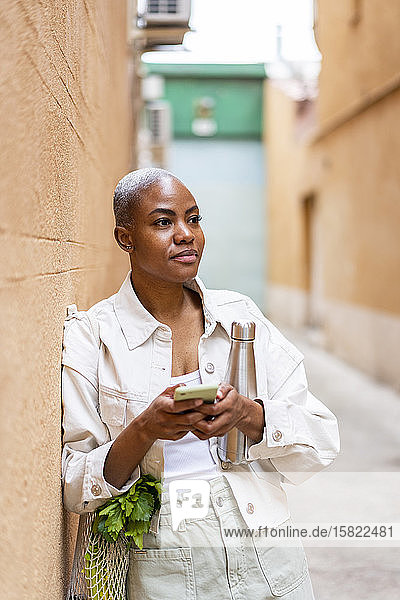 An eine Wand gelehnte Frau mit Thermoskanne  Lebensmitteln und Smartphone