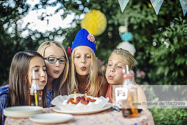 Mädchen feiern eine Geburtstagsparty im Freien und blasen Kerzen auf dem Kuchen aus