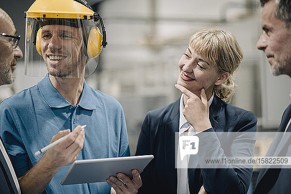 Geschäftsleute und lächelnder Arbeiter mit Tabletten im Gespräch in einer Fabrik