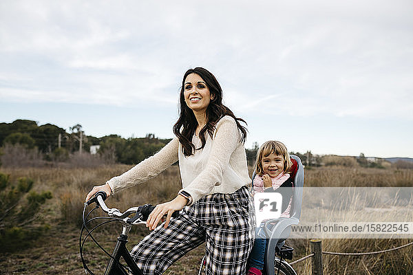 Frau fährt Fahrrad auf dem Land mit Tochter im Kindersitz