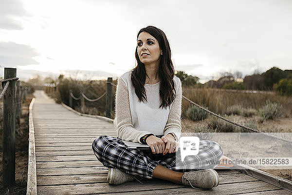 Woman sitting on a boardwalk in the countryside with laptop