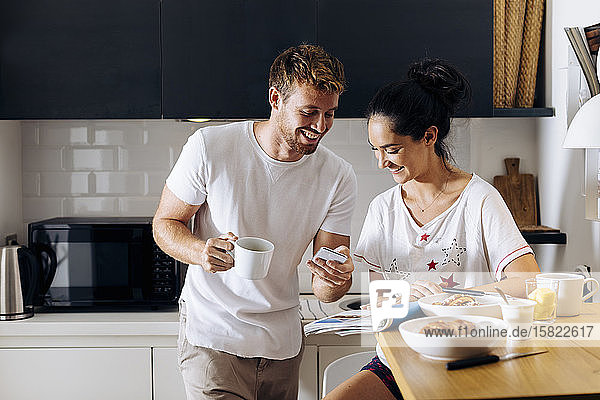 Happy young couple in the kitchen looking at cell phone