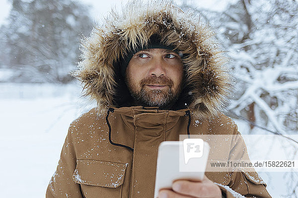 Portrait of pensive man with cell phone in winter