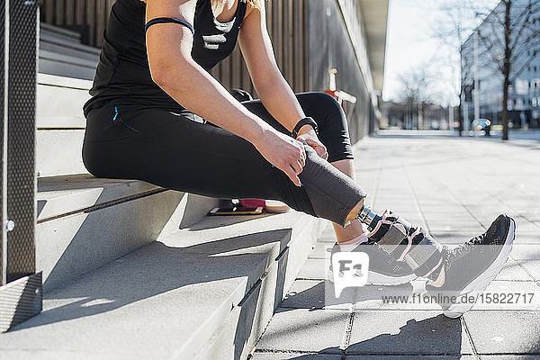 Sportliche junge Frau mit Beinprothese auf einer Treppe in der Stadt sitzend
