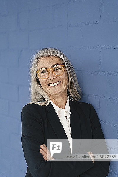 Porträt einer lächelnden grauhaarigen Geschäftsfrau  die an einer blauen Wand steht
