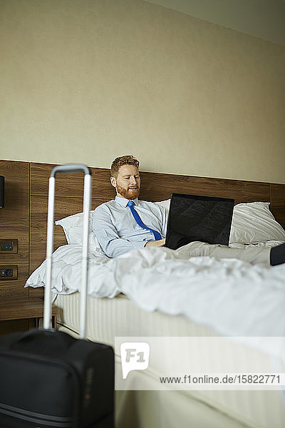 Geschäftsmann im Hotelzimmer auf dem Bett liegend mit Laptop