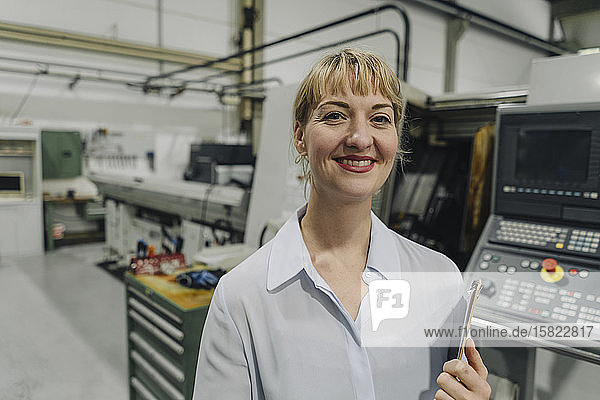 Porträt einer lächelnden Geschäftsfrau mit Klemmbrett in einer Fabrik