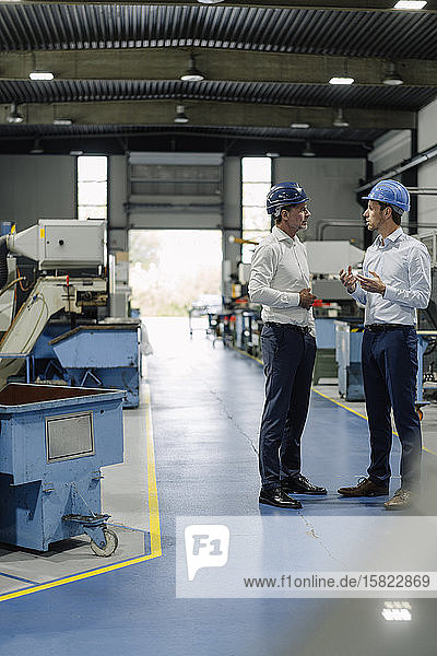 Two men wearing hard hats talking in a factory