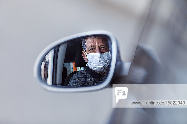 Spiegelung eines maskierten älteren Mannes im Außenspiegel eines Autos