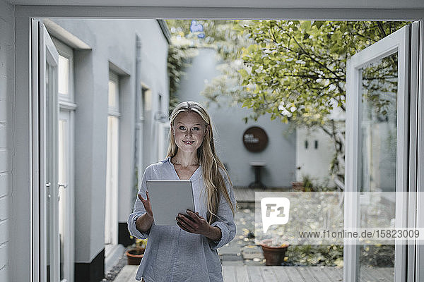 Porträt einer lächelnden jungen Frau  die mit einem Tablett an der Terrassentür steht