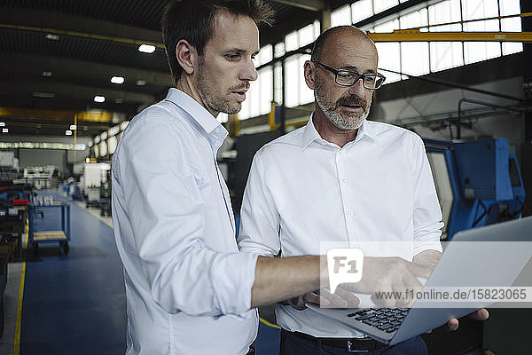 Two men using laptop in a factory