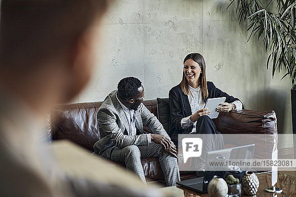 Lachender Geschäftsmann und Geschäftsfrau sitzen auf Couch in der Hotellobby